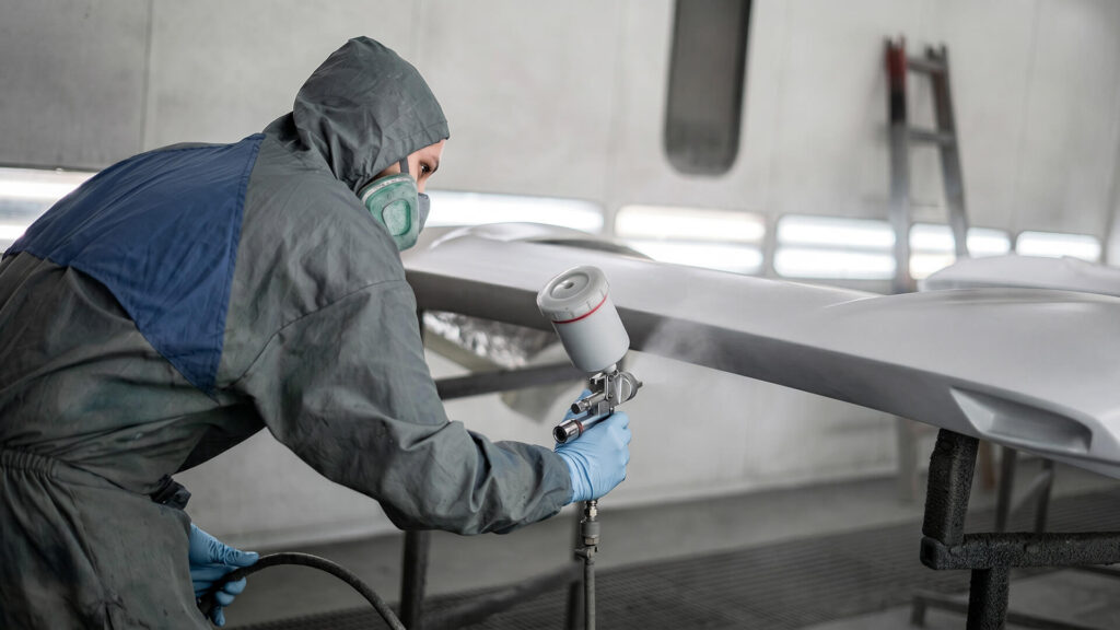 Professional worker applying powder coat to hanging metal parts