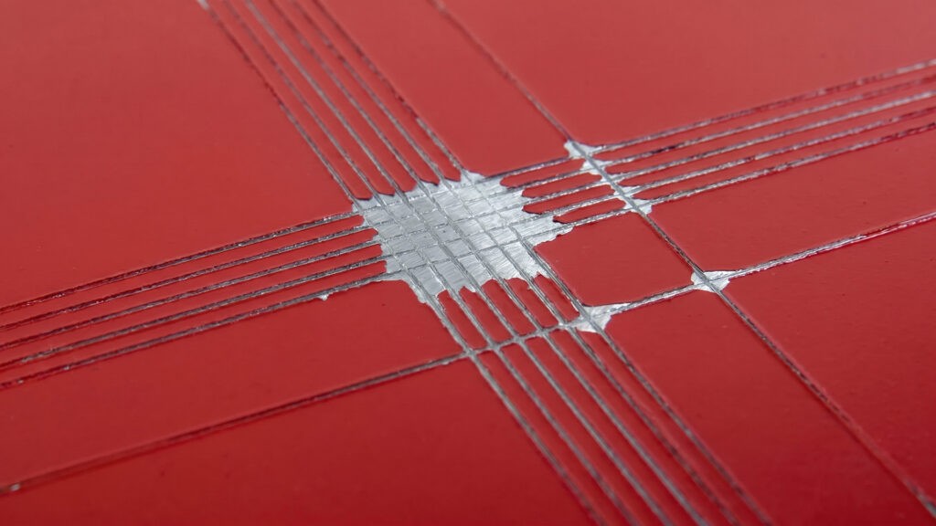 Worker performing cross-hatch tape test on painted metal part