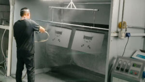 Worker powder coating metal parts in a factory