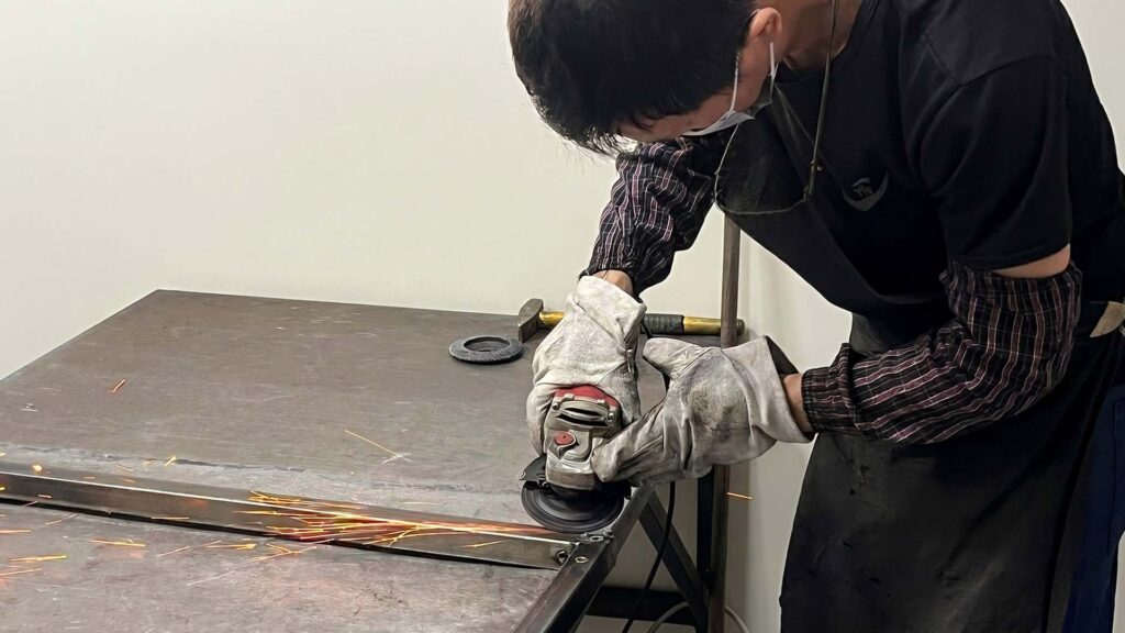 Worker using an angle grinder to prep metal for welding