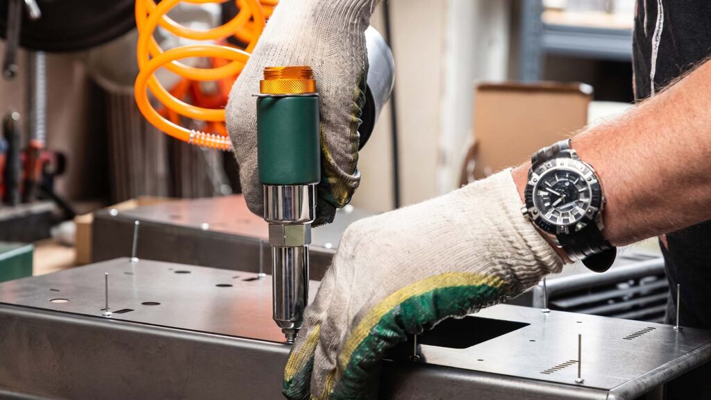 Worker using pneumatic rivet gun on sheet metal