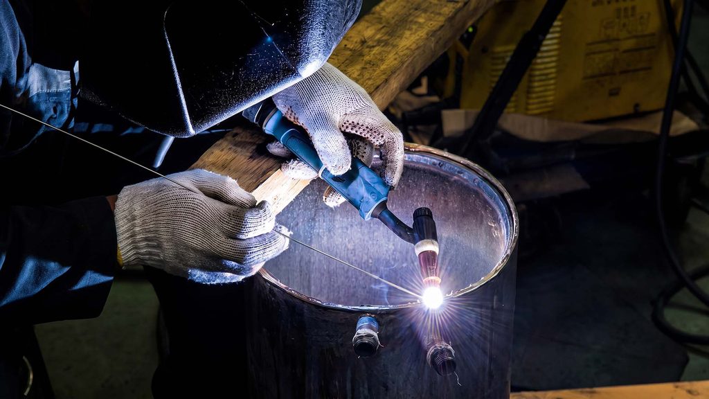 Hands performing TIG welding with filler rod