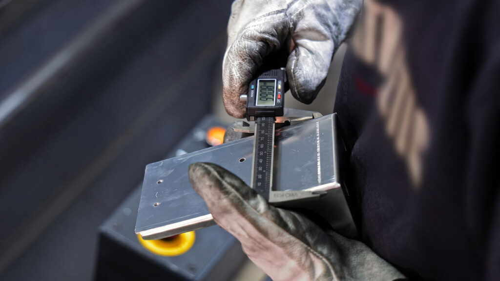 Inspector measuring sheet metal with digital caliper