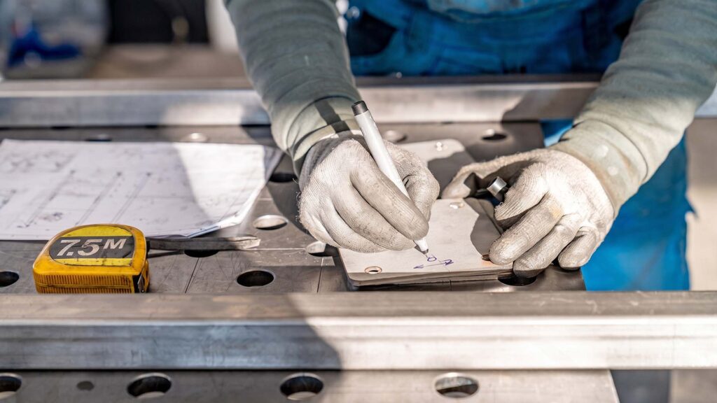 Worker marking sheet metal next to a blueprint