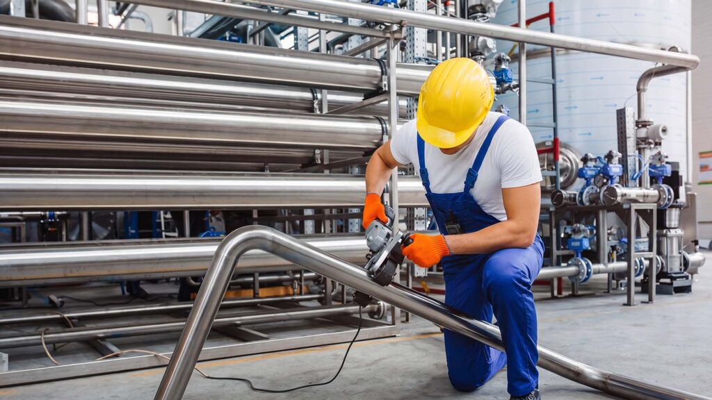 Worker polishing stainless steel pipe in industrial facility
